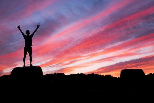 Person standing on rock as sun rises/sets