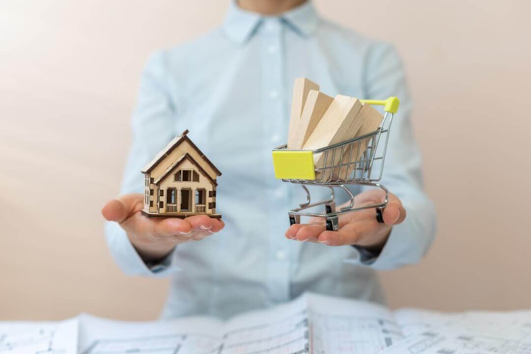 Person holding a small house in one hand and small cart in the other